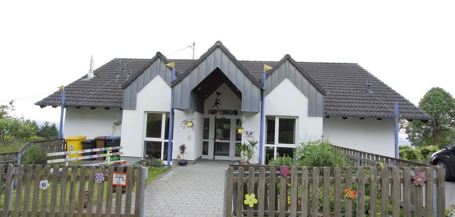 Kindergarten Luftikus Gebäudeansicht mit dem  Eingangsbereich umgeben mit einem Gartenzaun aus Holz dekoriert mit bunten Holzblüten 