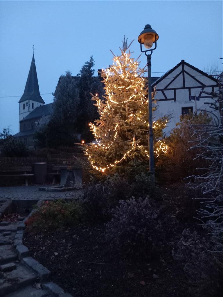 Weihnachtsbaum mit leuchtender Lichterkette im Hintergrund ist der Kirchturm